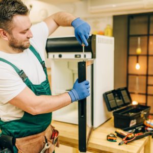 Worker with screwdriver repairs refrigerator door