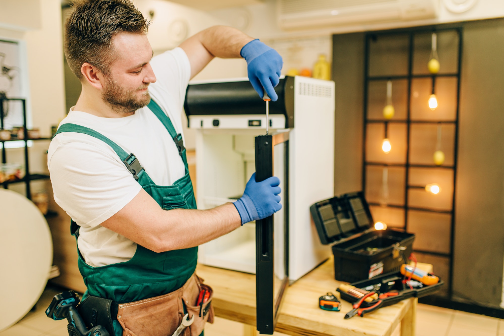 Worker with screwdriver repairs refrigerator door